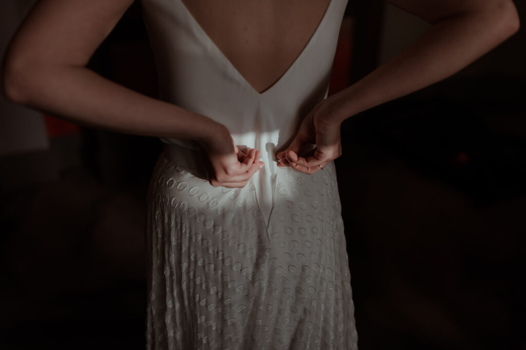 aesthetic and editorial wedding photography in London as bride does up her own dress in a beam of light